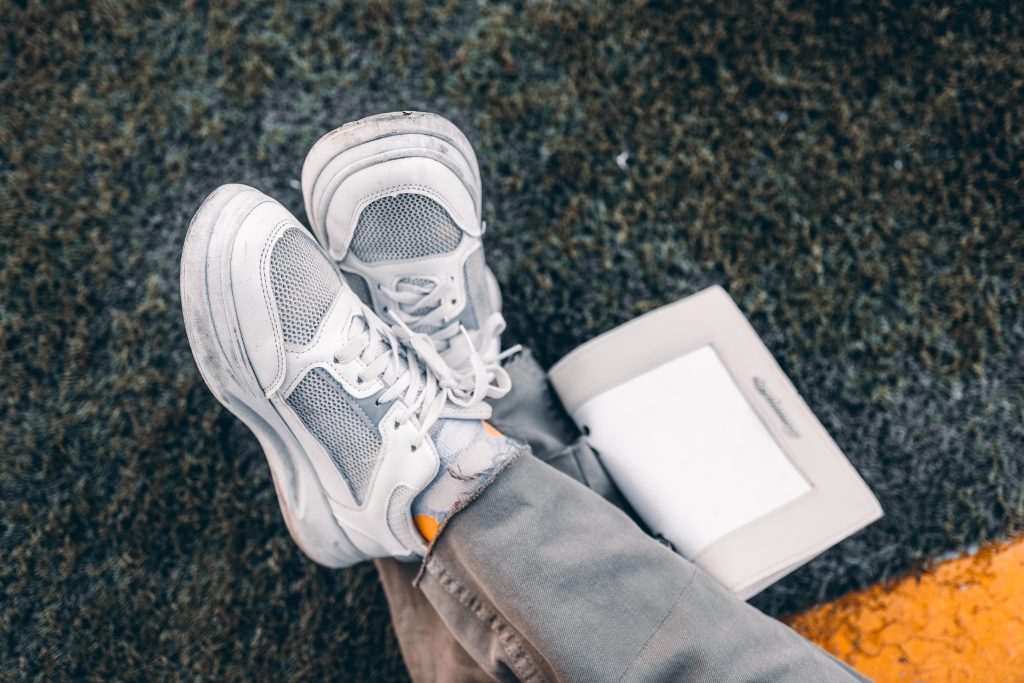 Witte sneakers op het gras naast een opengeslagen boek