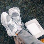 Witte sneakers op het gras naast een opengeslagen boek