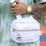 Hand houdt een witte crossbody tas met brede band vast