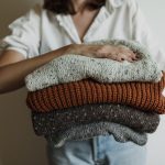 Vrouw houdt een stapel gebreide wollen truien vast