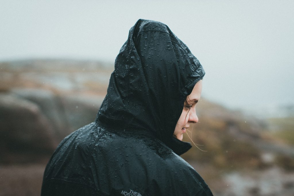 Persoon in een regenjas met de capuchon op in de regen