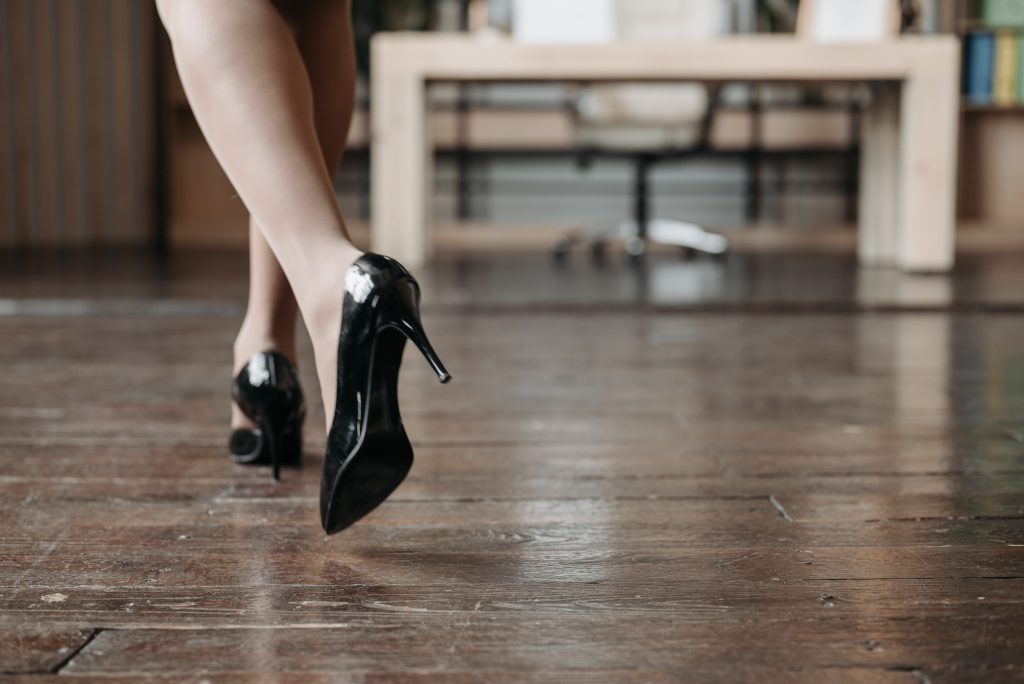 Vrouw loopt op zwarte pumps over een houten vloer