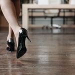 Vrouw loopt op zwarte pumps over een houten vloer