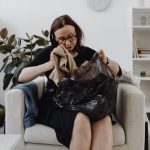 Vrouw sorteert kleding uit een zak in haar woonkamer